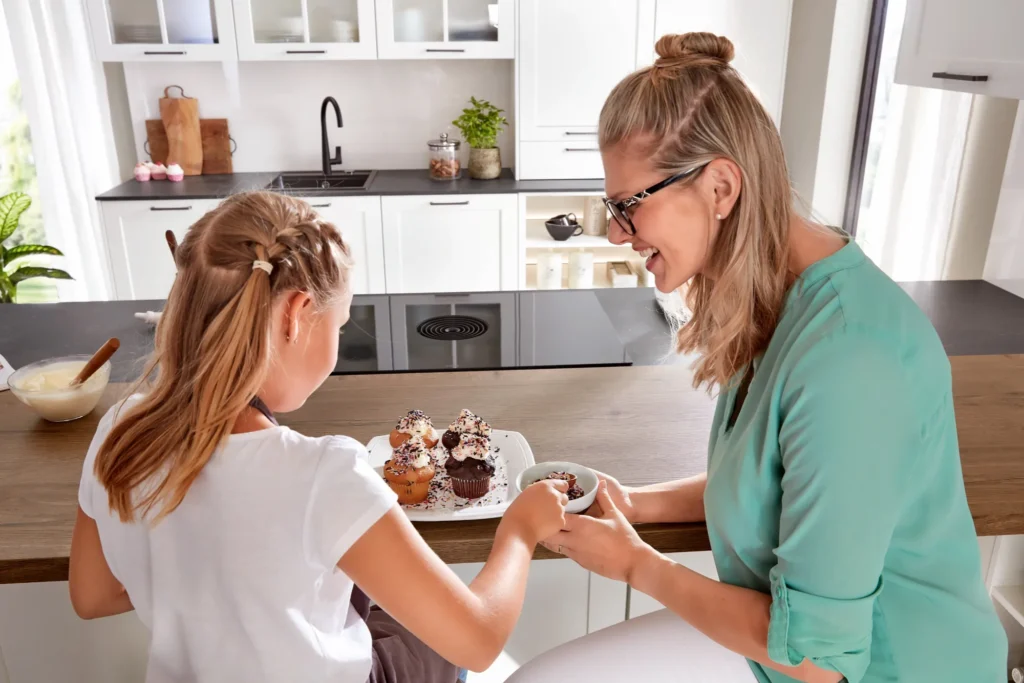 Mutter und Tochter dekorieren Cupcakes in moderner Küche mit Laminat-Arbeitsplatte