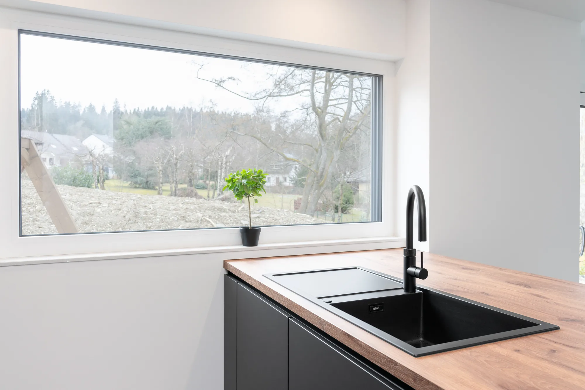 Pflegeleichtes schwarzes Komposit-Spülbecken mit Quooker-Wasserhahn auf einer stilvollen Holzoptik-Arbeitsplatte.