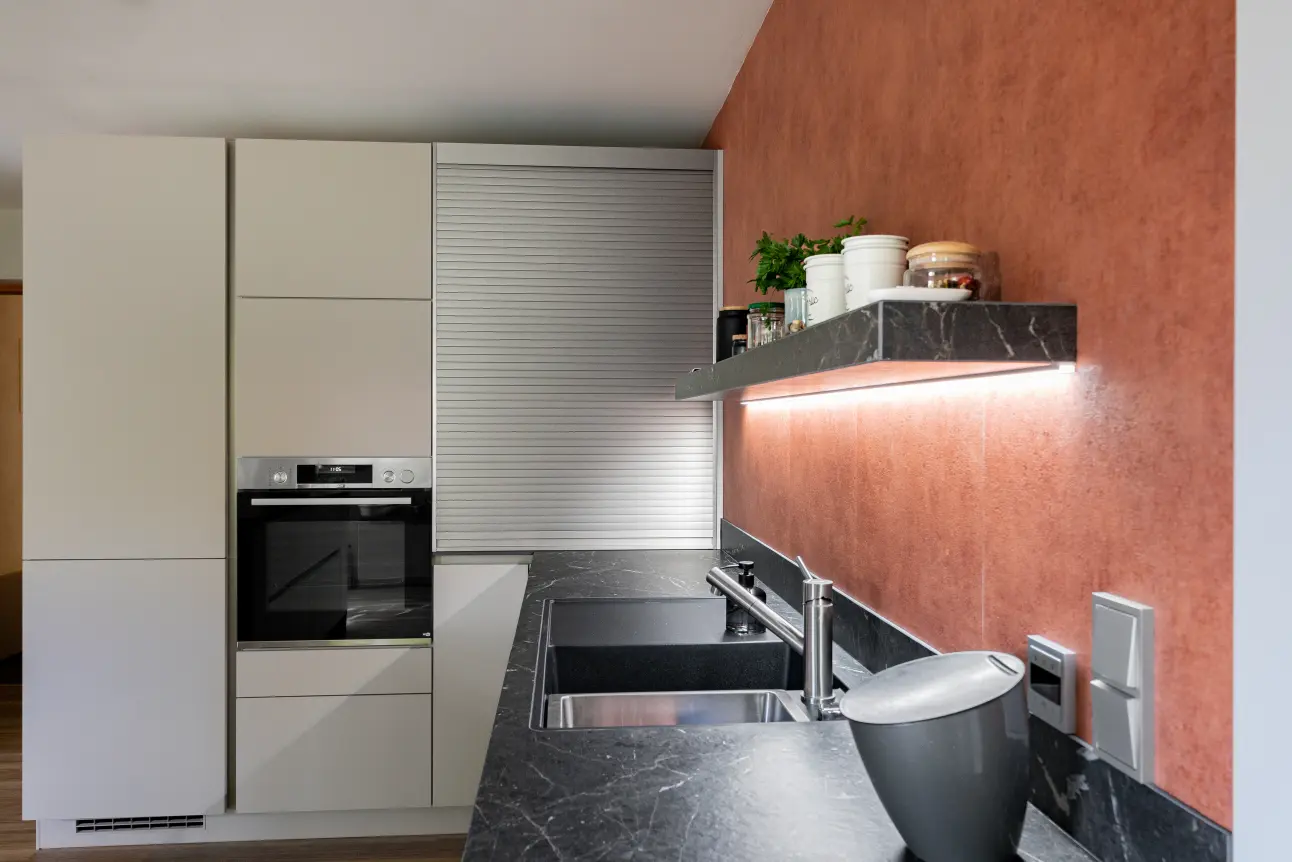 Spülbereich mit Doppelbecken, dunkler Marazzi Arbeitsplatte und LED-Regal in moderner Musterkueche.