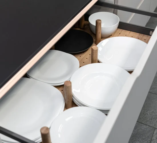 Offene Küchenschublade mit Holzstiften für sicheres Verstauen von Tellern und Schüsseln.