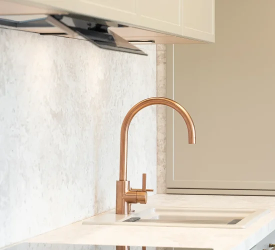 Kupferfarbene Armatur über weißem Spülbecken mit hellen Fronten